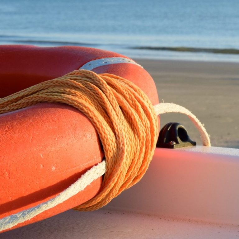 Rettungsring im Vordergrund und Strand mit Meer im Hintergrund